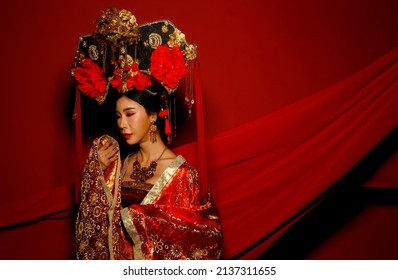 Dramatic Series Female Express Feeling Emotional With Fabric Fluttering In The Air. Asian Woman Wear China Royal Empress Traditional Costume With Golden Line Design Dress And Headwear, Red Background