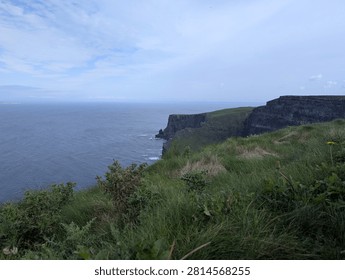 Dramatic sheer drop of the iconic cliffs meeting the Atlantic Ocean, viewed from a grassy clifftop on the west coast of Ireland.