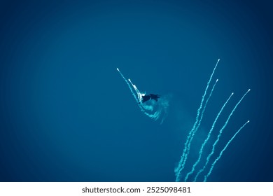 A dramatic shot of a fighter jet performing aerial maneuvers while releasing flares during a live airshow.
