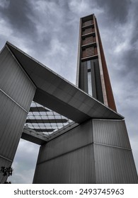 Dramatic shot of a modern tower with an angular archway against a cloudy sky, highlighting contemporary architectural design. Perfect for architecture, urban exploration, and dramatic themes.