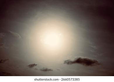 A dramatic shot of the sun surrounded by a soft glow and gentle clouds in a hazy sky. The scene evokes a sense of warmth, stillness, and natural light diffusion.