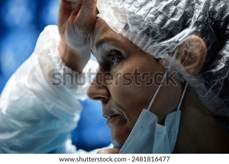Dramatic side view closeup of exhausted surgeon rubbing sweat of forehead while performing surgery in operating room copy space