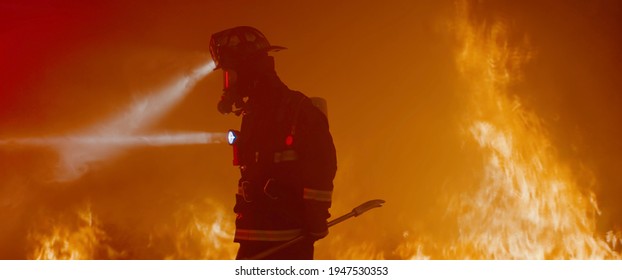 Dramatic silhouette of American firefighter in full gear exploring the huge fire zone - Shutterstock ID 1947530353