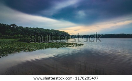 Dramatic sky after a rain storm over the beautiful green lily-pad covered Stone Lake on a summer evening, LaPorte, Indiana
