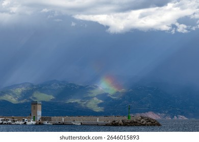 Dramatic sky after a storm, clouds over the Velebit Mountains in Croatia, a colorful rainbow breaks through the dark rain clouds