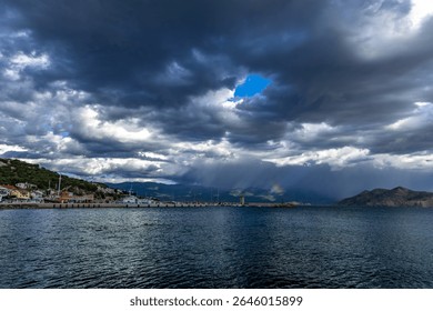 Dramatic sky after a storm, clouds over the Velebit Mountains in Croatia, a colorful rainbow breaks through the dark rain clouds