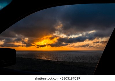 A dramatic sky appears in view from inside a car during evening time along the coast
