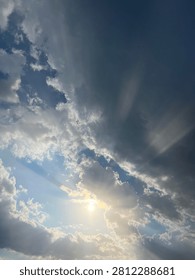 Dramatic sky with bright sun rays and crepuscular rays shining through dark storm clouds. Sunlight breaking through cloudy sky with blue sky and white clouds. Natural weather phenomenon, hope, faith and inspiration concept. High contrast cloudscape background with copy space. Perfect for design, banner, wallpaper and presentation.