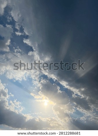 Dramatic sky with bright sun rays and crepuscular rays shining through dark storm clouds. Sunlight breaking through cloudy sky with blue sky and white clouds. Natural weather phenomenon, hope, faith and inspiration concept. High contrast cloudscape background with copy space. Perfect for design, banner, wallpaper and presentation.