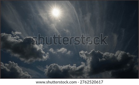 Dramatic sky with bright sun shining through dark cumulus and wispy cirrus clouds. High contrast landscape showing the power of nature and weather patterns in a deep blue sky.