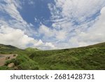 Dramatic sky with clouds over rolling green hills landscape.