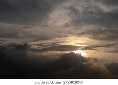 Dramatic sky with dark clouds and golden sunbeam piercing through. Sunlight glows softly behind heavy, textured clouds. Silhouetted storm clouds frame the fading golden light