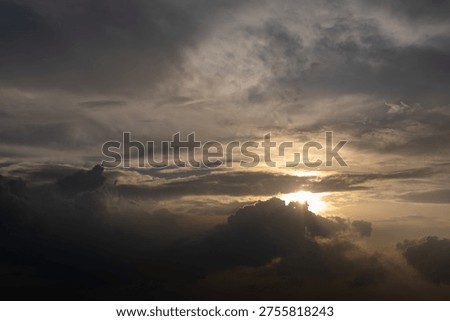 Dramatic sky with dark clouds and golden sunbeam piercing through. Sunlight glows softly behind heavy, textured clouds. Silhouetted storm clouds frame the fading golden light