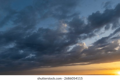 Dramatic sky with dark clouds illuminated by a warm sunset glow creates a stunning visual effect. Perfect for backgrounds, nature, and weather-themed projects.