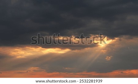 Dramatic sky with dark clouds and sun rays breaking through, creating a warm glow.