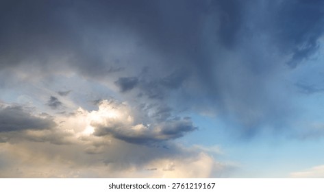 Dramatic sky with dark storm clouds and bright sun peeking through. Blue sky contrasts with ominous grey clouds. Light breaks through cloud layers, creating rays