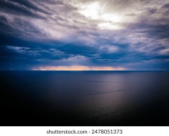 A dramatic sky with dark, stormy clouds over a tranquil sea at sunset, featuring a striking yellow and orange horizon. The image captures the contrast between the calm water and the turbulent sky. - Powered by Shutterstock