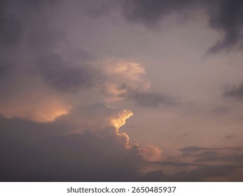 A dramatic sky during sunset with dark clouds and soft golden light peeking through.