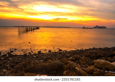 dramatic sky during sunset with rocks and boats foreground in Bangkalan, Madura, Indonesia.