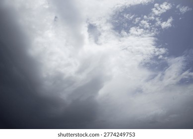 A dramatic sky featuring a blend of dark, heavy storm clouds and bright, wispy white clouds, with glimpses of blue sky. This atmospheric scene captures the changing weather and natural beauty.