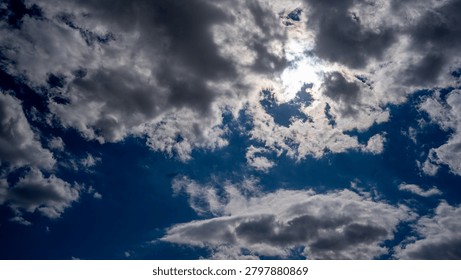 A dramatic sky filled with billowing clouds partially obscuring the bright sun, creating a stunning interplay of light and shadow.