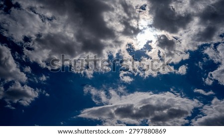 A dramatic sky filled with billowing clouds partially obscuring the bright sun, creating a stunning interplay of light and shadow.