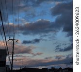 A dramatic sky filled with dark clouds and pastel-toned sunset light over rooftops and power lines in a quiet urban neighborhood.