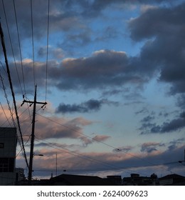 A dramatic sky filled with dark clouds and pastel-toned sunset light over rooftops and power lines in a quiet urban neighborhood.