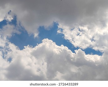 A dramatic sky filled with thick, fluffy clouds revealing a bright patch of blue sky in the center. The contrast between the dark gray clouds and the illuminated white clouds creates a dynamic and atmospheric scene, capturing the beauty of natural weather patterns and the ever-changing sky.