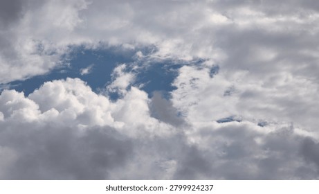 A dramatic sky filled with thick grey storm clouds and fluffy white cumulus clouds parting, revealing a glimpse of clear blue sky in the center. Perfect for backgrounds, weather concepts, or themes of hope and change