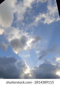 A dramatic sky filled with towering dark clouds and bright sunlight streaming through openings in the clouds, creating beautiful crepuscular rays against a vibrant blue sky. Natural weather background with a peaceful and majestic atmosphere.