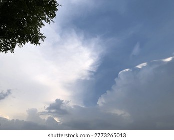 A dramatic sky with large, fluffy white clouds and dark storm clouds gathering, with a hint of green foliage in the upper left corner.