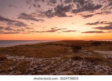 Dramatic sky over a large beach and grassy sand dunes at dusk in autumn