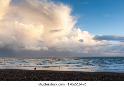 Dramatic sky with rainclouds over the sea in the evening and a lonely couple of people walking near the water's edge in the distance. Storm coming towards Brighton beach.