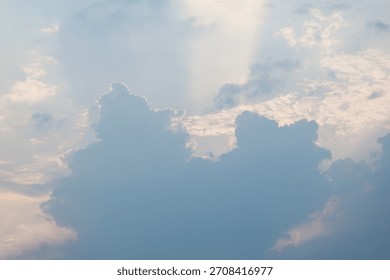 A dramatic sky scene dominated by large, dense cumulus clouds, their blue-grey masses silhouetted and highlighted by bright, soft rays of sunlight breaking through from above during sunrise or sunset
