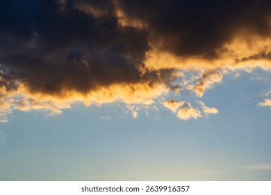 A dramatic sky scene featuring dark storm clouds highlighted by golden sunlight above a tranquil blue horizon, evoking contrast, atmosphere, and natural beauty.