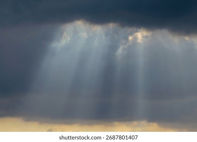 Dramatic sky with sunbeams shining through dark storm clouds. Beautiful natural light phenomenon creating contrast between darkness and hope. Ideal for nature backgrounds, inspirational themes, enviro