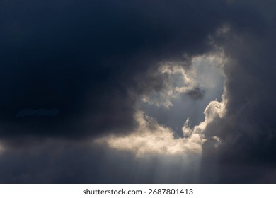 Dramatic sky with sunbeams shining through dark storm clouds. Beautiful natural light phenomenon creating contrast between darkness and hope. Ideal for nature backgrounds, inspirational themes, enviro