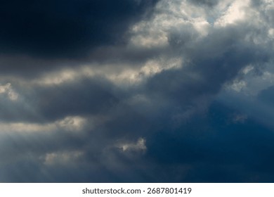 Dramatic sky with sunbeams shining through dark storm clouds. Beautiful natural light phenomenon creating contrast between darkness and hope. Ideal for nature backgrounds, inspirational themes, enviro