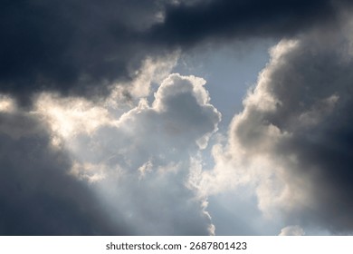 Dramatic sky with sunbeams shining through dark storm clouds. Beautiful natural light phenomenon creating contrast between darkness and hope. Ideal for nature backgrounds, inspirational themes, enviro