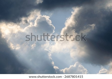 Dramatic sky with sunbeams shining through dark storm clouds. Beautiful natural light phenomenon creating contrast between darkness and hope. Ideal for nature backgrounds, inspirational themes, enviro