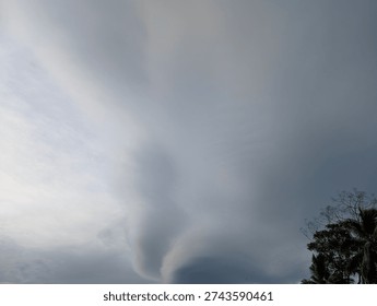 A dramatic sky with swirling clouds, hinting at a storm or unusual weather phenomenon, with trees silhouetted against the turbulent atmosphere.