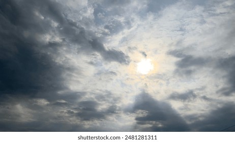 A dramatic sky with thick clouds partially covering the sun, creating a captivating play of light and shadows. The sun’s rays break through the cloud cover, casting a soft glow.