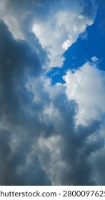 Dramatic sky with thick dark storm clouds contrasting against bright blue patches and fluffy white clouds. Dynamic weather scene showing cloud formation and natural light breaking through. Ideal for weather, atmosphere, and dramatic background themes