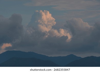 Dramatic sky with towering cumulus clouds illuminated by soft golden light over distant, dark mountain silhouettes at sunset.