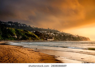 Dramatic sky with warm sunset light illuminates the coastline and homes nestled on the Palos Verdes hills overlooking Redondo Beach