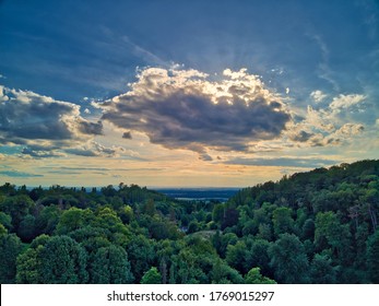 dramatic sky where the sun breaks dramatically through the cloud cover with a beautiful hill in the background and green trees and bushes in the foreground
