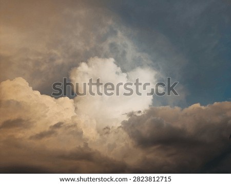A dramatic skyscape featuring a large, fluffy cumulus cloud illuminated by warm golden sunlight against contrasting dark, moody storm clouds. Perfect for nature backgrounds and atmospheric designs.