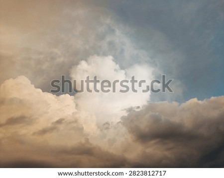 A dramatic skyscape featuring a large, fluffy cumulus cloud illuminated by warm golden sunlight against contrasting dark, moody storm clouds. Perfect for nature backgrounds and atmospheric designs.