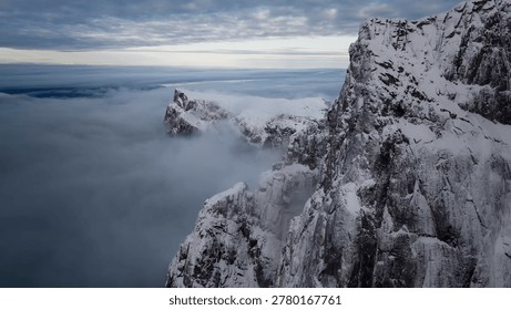 Dramatic snow-covered mountain cliffs rising above a thick, mysterious blanket of white clouds and fog